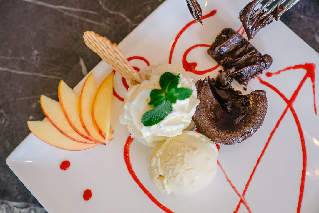 Plate with sliced apples, vanilla ice cream, whipped cream topped with mint, and a chocolate lava cake with a fork holding a piece.