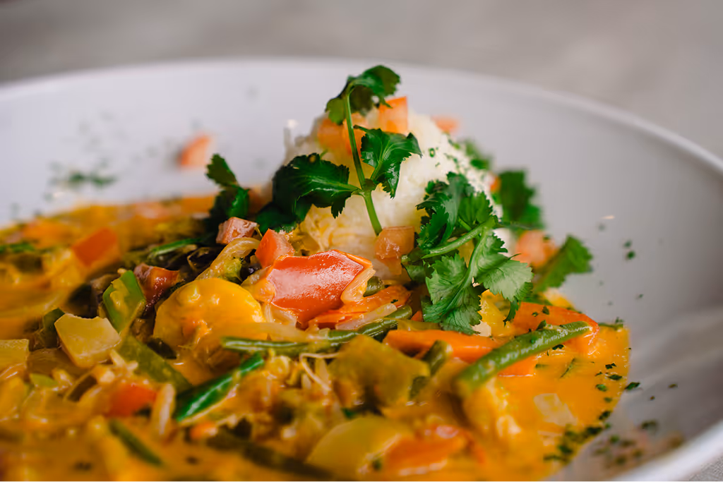 Plate of vegetable curry with rice garnished with fresh cilantro on a white dish.