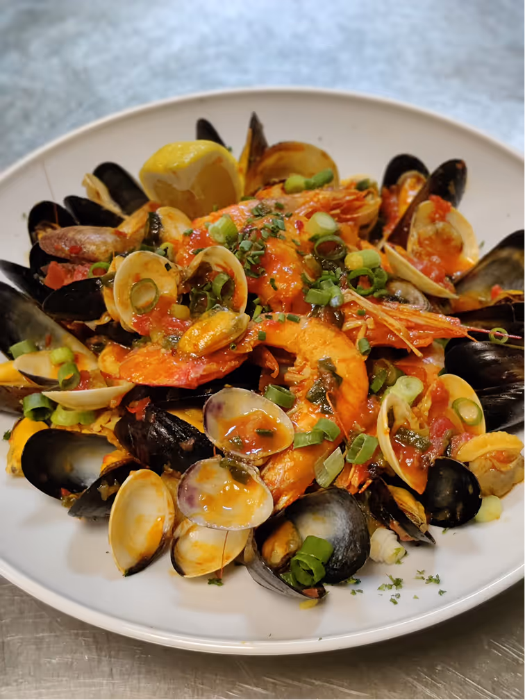 Plate of seafood paella with shrimp, mussels, clams, garnished with chopped green onions and a lemon wedge.